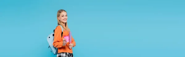 Estudante sorrindo com copo de papel e laptop olhando para a câmera isolada em azul, banner — Fotografia de Stock