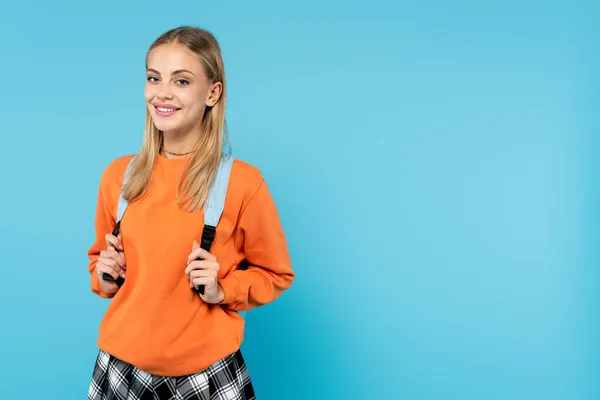 Estudiante sonriente en sudadera sosteniendo mochila aislada en azul - foto de stock