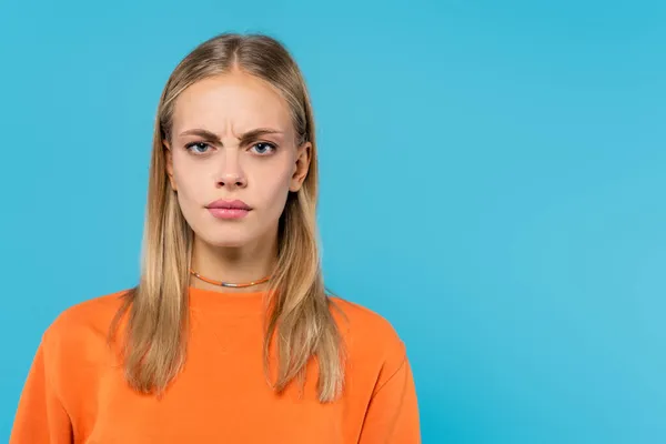 Mujer rubia ofendida en sudadera naranja mirando a la cámara aislada en azul - foto de stock