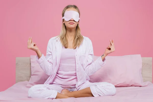 Молода жінка в масці для сну і піжамі, роздумуючи на ліжку ізольована на рожевому — стокове фото