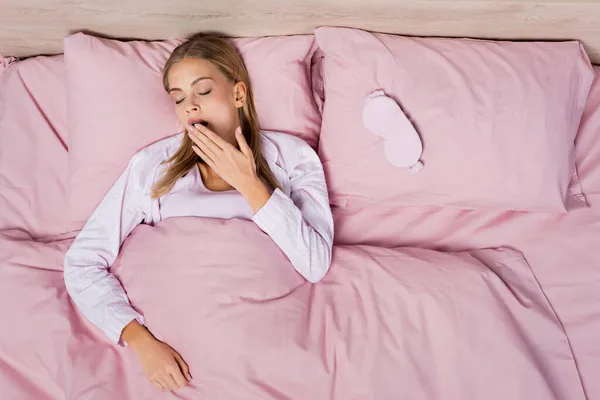 Top view of woman yawning near sleep mask on bed — Stock Photo