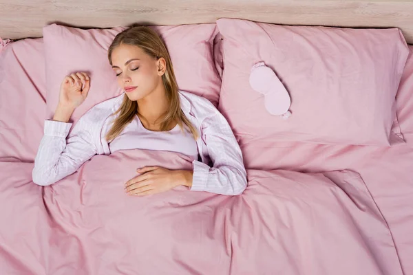 Vista dall'alto della donna che dorme vicino alla maschera sui cuscini sul letto — Foto stock