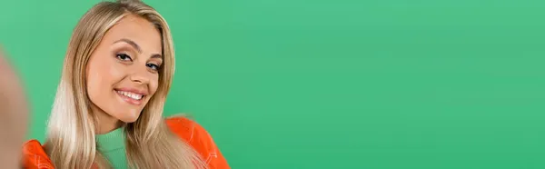 Joyful blonde woman looking at camera while smiling isolated on green, banner — Stock Photo