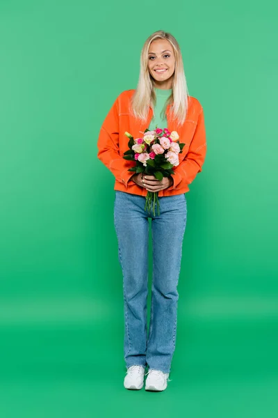 Vue pleine longueur de la femme blonde élégante tenant bouquet coloré sur vert — Photo de stock