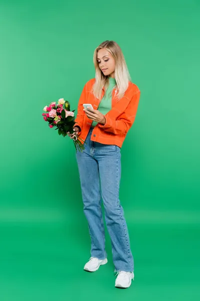 Vista completa de la mujer rubia de moda con mensajes de ramo en el teléfono inteligente en verde - foto de stock