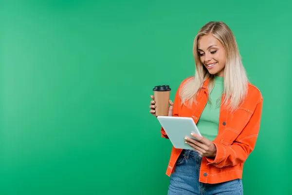 Heureuse femme blonde avec boisson à emporter en regardant tablette numérique isolé sur vert — Photo de stock