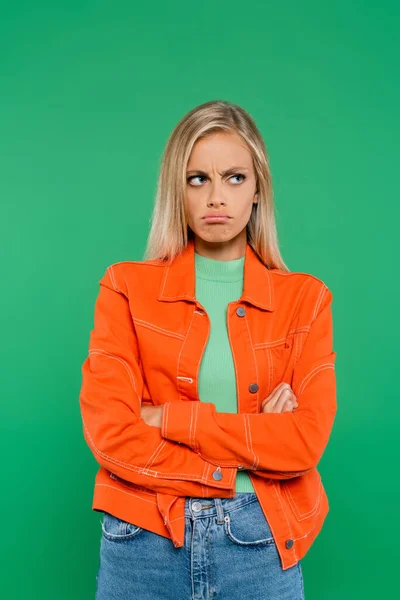 Offended woman frowning and pouting lips while standing with crossed arms isolated on green — Stock Photo