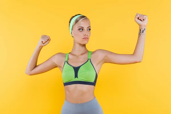 Mujer confiada en ropa deportiva mirando hacia otro lado mientras se calienta aislado en amarillo - foto de stock