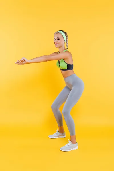 Vista completa de la mujer joven y deportiva haciendo sentadas en amarillo - foto de stock