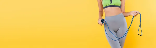 Partial view of sportive woman with skipping rope standing isolated on yellow, banner — Stock Photo