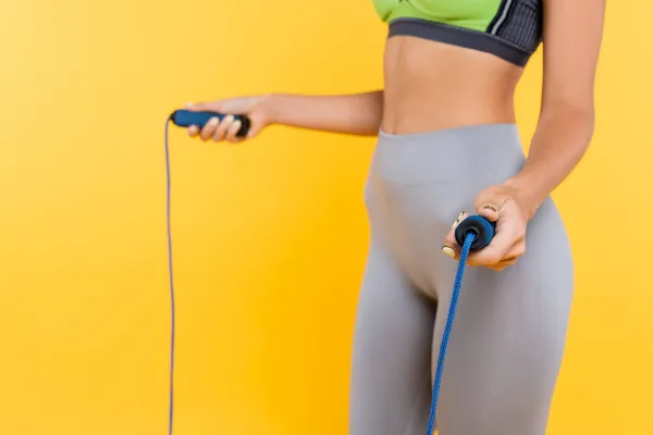 Cropped view of blurred sportswoman in grey leggings training with jump rope isolated on yellow — Stock Photo