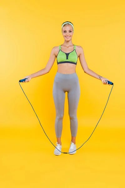 Vue pleine longueur de la jeune femme dans l'entraînement de vêtements de sport avec corde à sauter sur jaune — Photo de stock