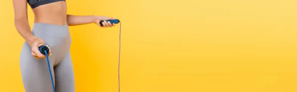 Vista recortada de la deportista en leggings grises sosteniendo cuerda de salto aislado en amarillo, bandera - foto de stock