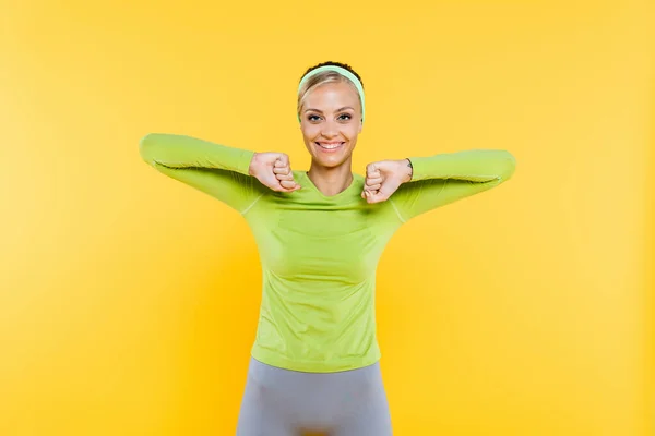 Mulher esportiva sorrindo para a câmera enquanto aquece isolado no amarelo — Fotografia de Stock