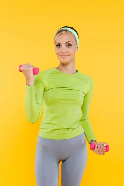 Счастливая женщина в зеленых футболках с длинными рукавами тренировки с гантели изолированы на желтый — стоковое фото