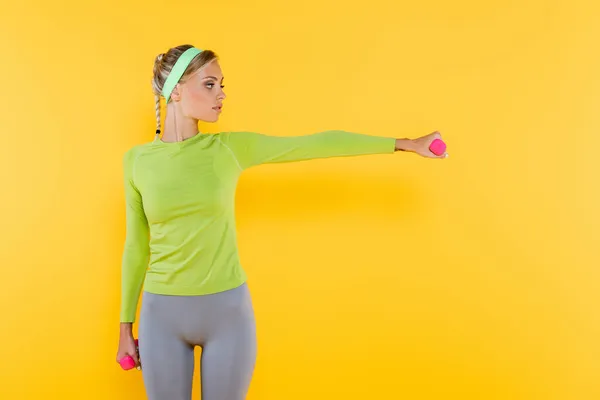 Jeune femme en t-shirt vert à manches longues avec haltères isolées sur jaune — Photo de stock