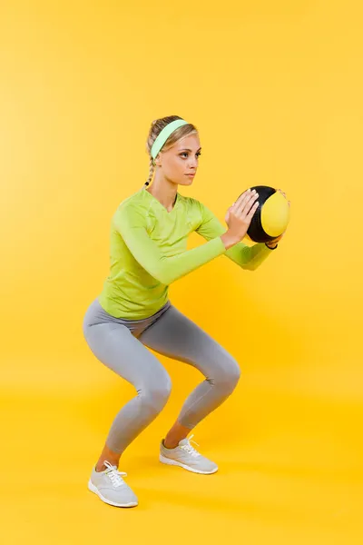 Full length view of slim woman in grey leggings doing sit ups with ball on yellow — Stock Photo