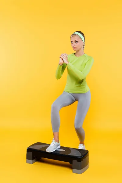 Piena vista lunghezza della donna magra con le mani serrate formazione sul bordo passo su giallo — Foto stock