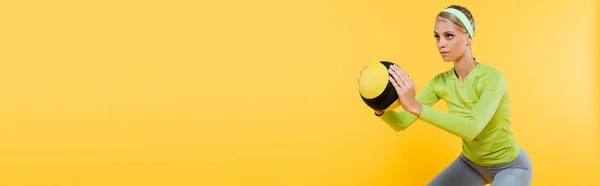 Young woman in green long sleeve t-shirt exercising with ball isolated on yellow, banner — Stock Photo