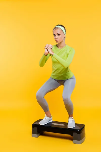 Sportswoman with clenched hands doing sit ups on step board on yellow — Stock Photo