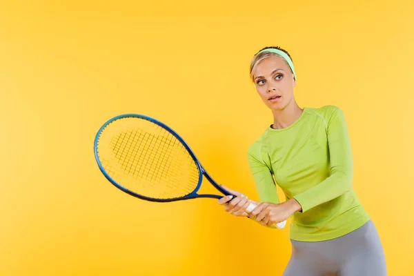 Молода жінка в зеленій футболці з довгим рукавом грає в теніс ізольовано на жовтому — стокове фото