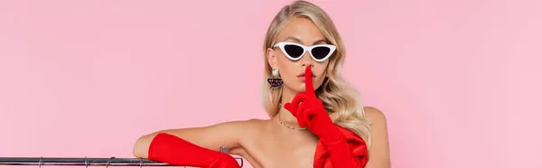 Glamour woman in sunglasses and red gloves showing hush sign isolated on pink, banner — Stock Photo