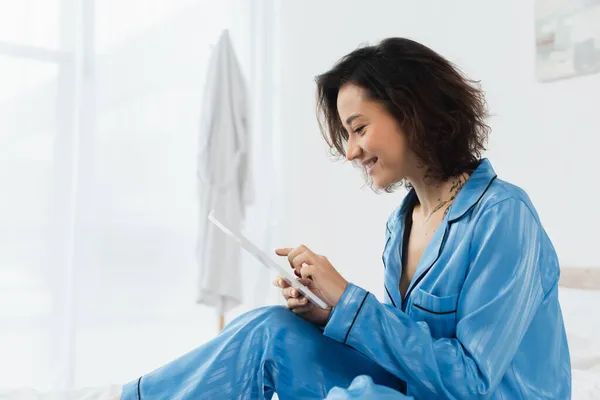 Glückliche junge Frau im blauen Schlafanzug mit digitalem Tablet zu Hause — Stockfoto