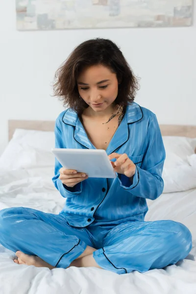 Mujer joven en pijama azul usando tableta digital en casa - foto de stock