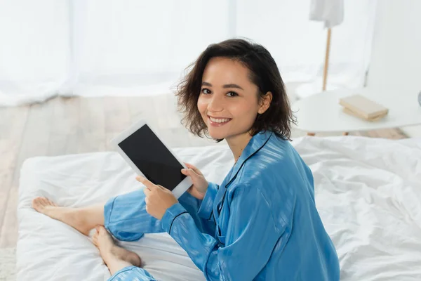 Vue grand angle de jeune femme heureuse en pyjama bleu en utilisant une tablette numérique dans la chambre — Photo de stock
