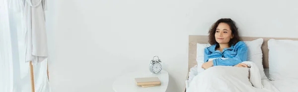 Брюнетка женщина лежит в постели возле прикроватного столика с книгами и будильником, баннер — стоковое фото