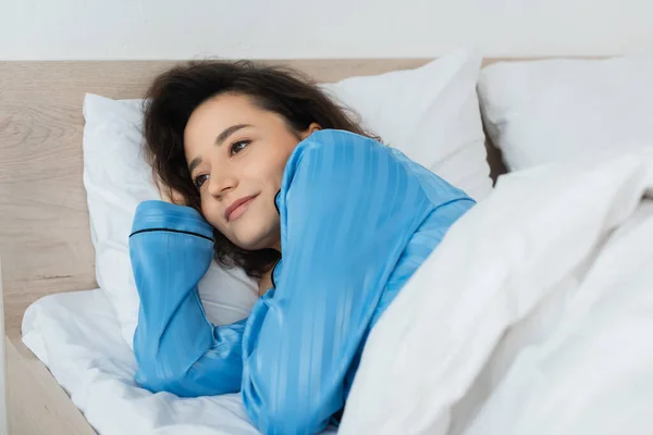 Brunette woman in blue pajamas lying on bed — Stock Photo