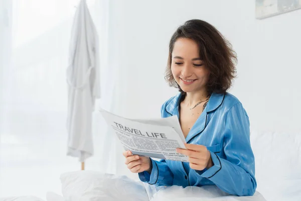 Happy woman in blue pajamas reading travel life newspaper in bed — Stock Photo