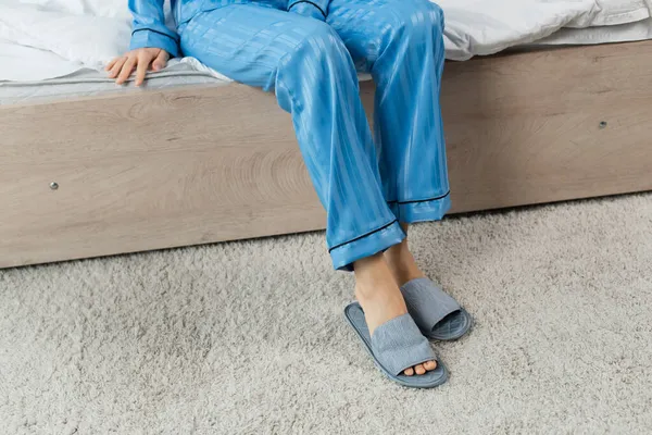 Cropped view of young woman in blue pajamas wearing slippers in bedroom — Stock Photo