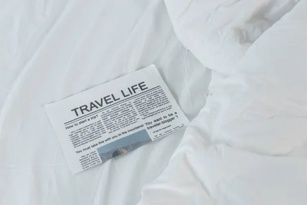 Vista de ángulo alto del periódico de la vida del viaje en la cama blanca - foto de stock