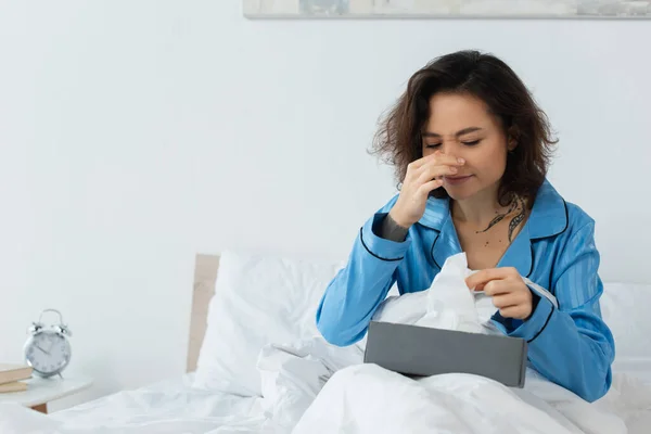 Sick woman with running nose reaching tissue box in bed — Stock Photo