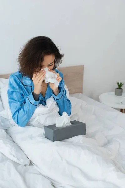 Sick woman sneezing in tissue in bedroom — Stock Photo