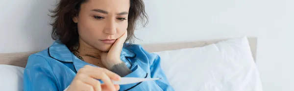 Mujer joven enferma mirando termómetro electrónico, bandera - foto de stock