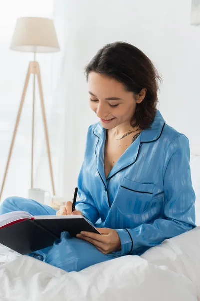 Happy young woman writing in notebook in bedroom — Stock Photo