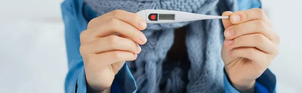 Vue recadrée de la femme malade en écharpe tricotée tenant thermomètre électronique, bannière — Photo de stock
