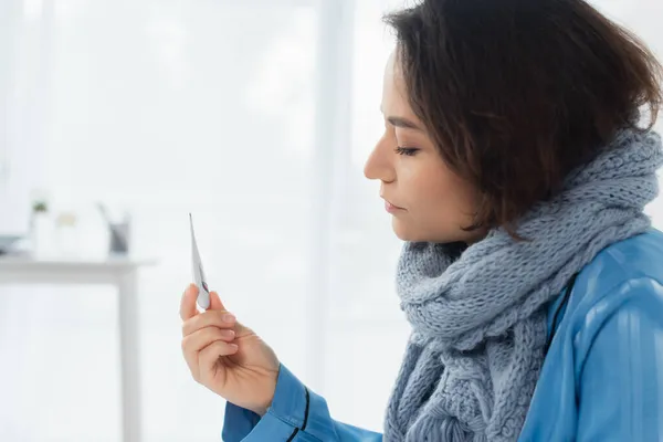 Malade jeune femme en écharpe tricotée bleue tenant thermomètre électronique — Photo de stock