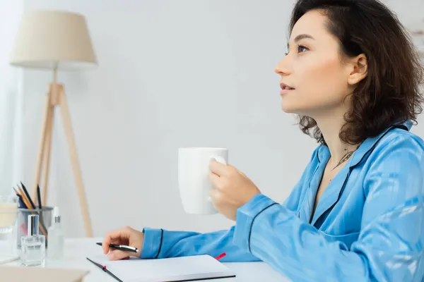 Mujer pensativa sosteniendo una taza de café y pensando en casa - foto de stock