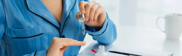 Cropped view of young woman holding pipette with oil near fingernails, banner — Stock Photo