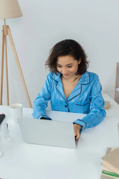 Bruna giovane freelance utilizzando laptop vicino a tazza e libri — Foto stock