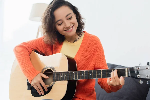 Heureuse jeune femme jouant de la guitare acoustique à la maison — Photo de stock