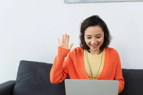 Happy young operator in headset waving hand during video call — Stock Photo