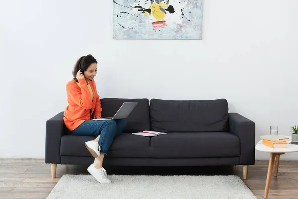 Cheerful operator in headset using laptop while sitting on sofa — Stock Photo