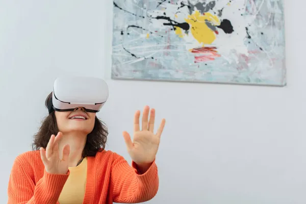 Young happy woman in vr headset gesturing during simulation game at home — Stock Photo