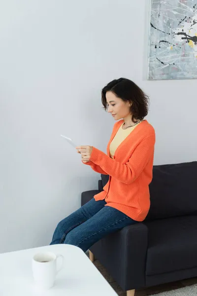 Junge Frau nutzt digitales Tablet und lehnt sich auf Couch an — Stockfoto