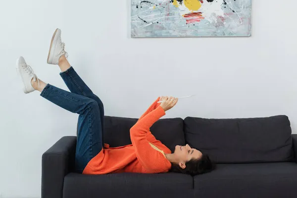 Joyeuse jeune femme en utilisant une tablette numérique et couché sur le canapé — Photo de stock