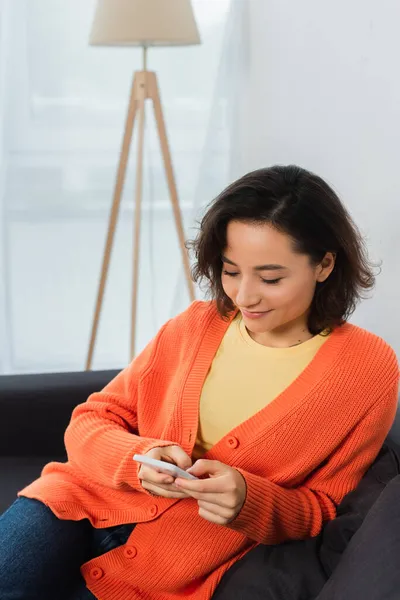 Счастливая молодая женщина текстурирует на мобильном телефоне в гостиной — стоковое фото